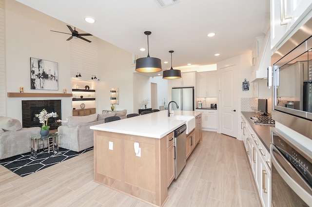 kitchen with hanging light fixtures, stainless steel appliances, a brick fireplace, an island with sink, and white cabinets