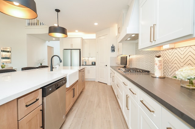 kitchen featuring white cabinetry, sink, hanging light fixtures, premium range hood, and appliances with stainless steel finishes