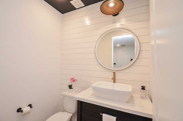 bathroom featuring vanity, toilet, and wooden walls