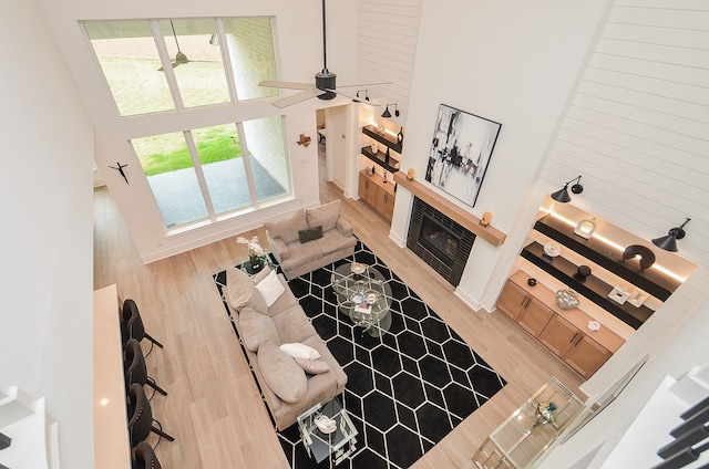 living room with a tiled fireplace, ceiling fan, wood-type flooring, and a high ceiling