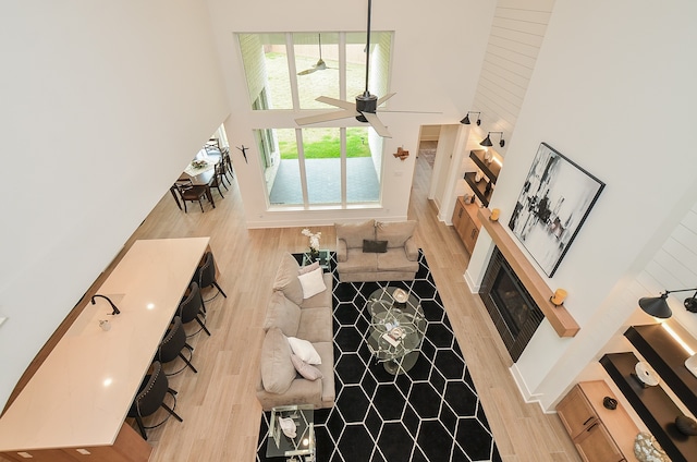 living room featuring a fireplace, a high ceiling, light hardwood / wood-style floors, and ceiling fan