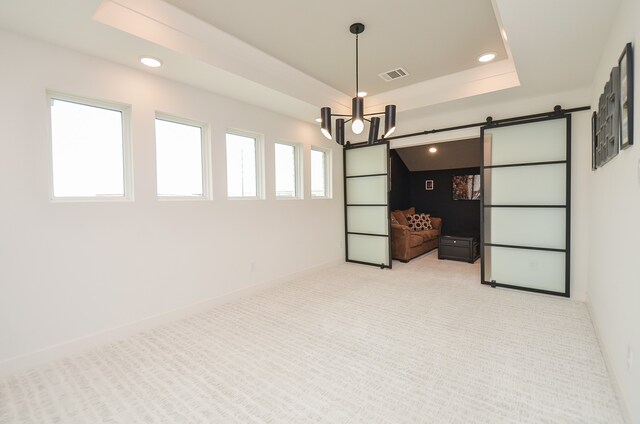 carpeted spare room with a tray ceiling, a barn door, and a notable chandelier