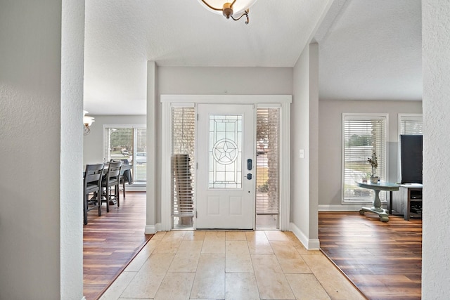 foyer entrance with light hardwood / wood-style floors, a textured ceiling, a wealth of natural light, and a chandelier