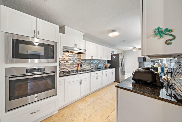 kitchen featuring dark stone counters, a textured ceiling, tasteful backsplash, white cabinetry, and stainless steel appliances