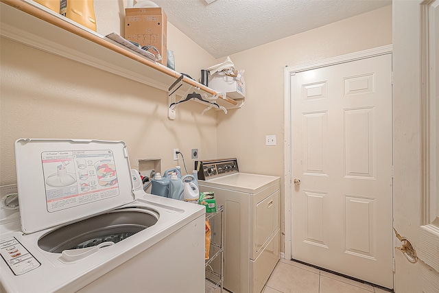 clothes washing area featuring washer and clothes dryer, light tile patterned floors, and a textured ceiling