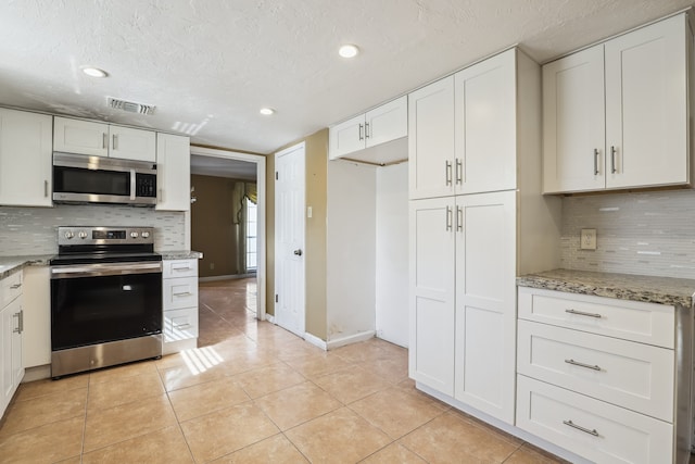 kitchen featuring light stone counters, a textured ceiling, light tile patterned floors, stainless steel appliances, and white cabinets