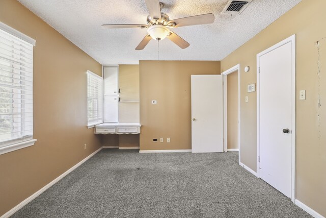 unfurnished bedroom featuring ceiling fan, carpet, multiple windows, and a textured ceiling