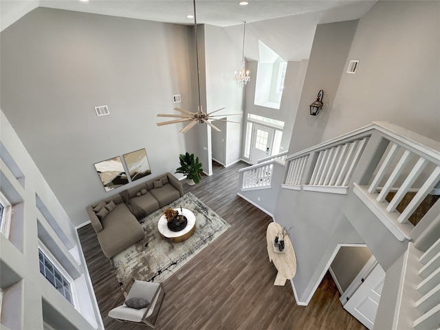 unfurnished living room with ceiling fan with notable chandelier, dark wood-type flooring, and high vaulted ceiling