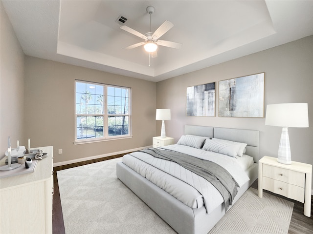 bedroom featuring hardwood / wood-style floors, ceiling fan, and a raised ceiling