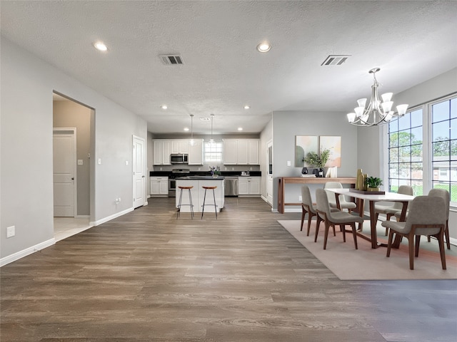 kitchen with a center island, appliances with stainless steel finishes, white cabinetry, wood-type flooring, and a chandelier