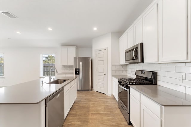 kitchen with white cabinets, sink, light hardwood / wood-style flooring, an island with sink, and appliances with stainless steel finishes