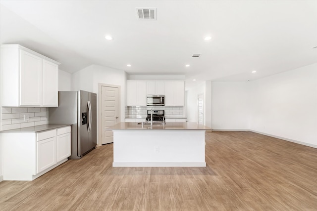 kitchen with decorative backsplash, light wood-type flooring, stainless steel appliances, white cabinetry, and an island with sink