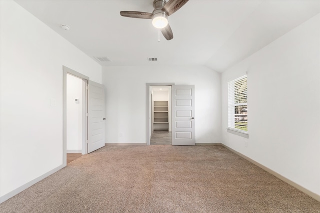 unfurnished bedroom featuring light carpet, a walk in closet, vaulted ceiling, ceiling fan, and a closet