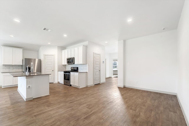 kitchen featuring white cabinets, light wood-type flooring, stainless steel appliances, and a center island with sink