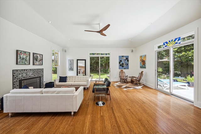 living room with ceiling fan, wood-type flooring, a wealth of natural light, and a tiled fireplace