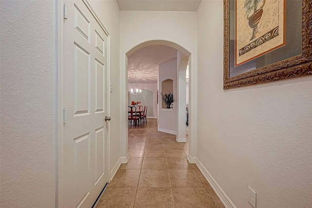 corridor featuring light tile patterned floors, baseboards, arched walkways, and an inviting chandelier