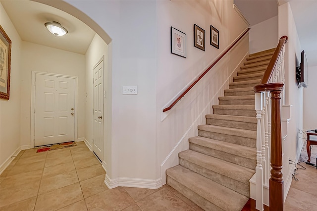 stairs featuring baseboards, arched walkways, and tile patterned flooring