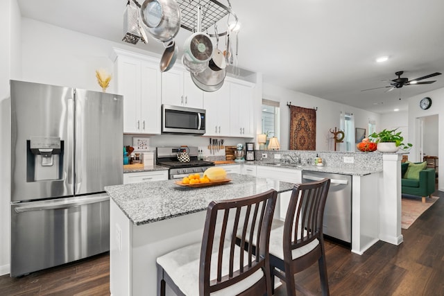 kitchen with kitchen peninsula, stainless steel appliances, dark wood-type flooring, sink, and a center island