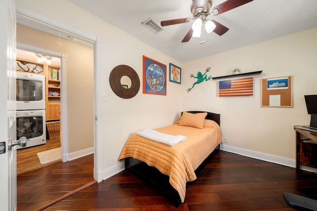 bedroom with ceiling fan, stacked washer / dryer, and dark wood-type flooring