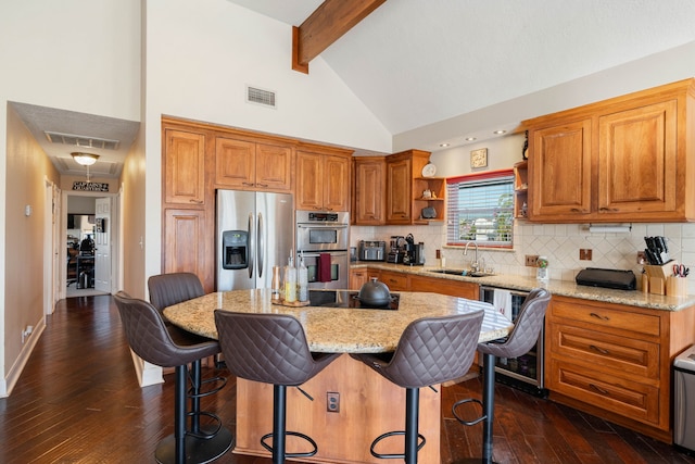 kitchen with dark hardwood / wood-style flooring, stainless steel appliances, sink, beamed ceiling, and a center island