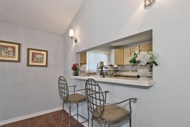 kitchen with dark wood-type flooring, backsplash, lofted ceiling, a kitchen bar, and light brown cabinetry