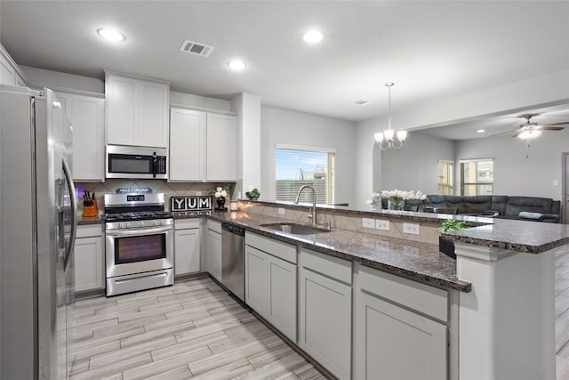 kitchen with kitchen peninsula, stainless steel appliances, sink, pendant lighting, and white cabinetry