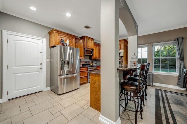 kitchen featuring a breakfast bar, dark stone counters, crown molding, light tile patterned floors, and appliances with stainless steel finishes