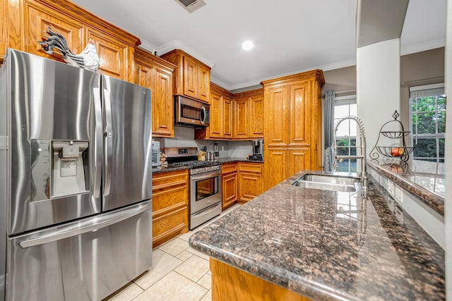 kitchen with appliances with stainless steel finishes, ornamental molding, sink, light tile patterned floors, and dark stone countertops