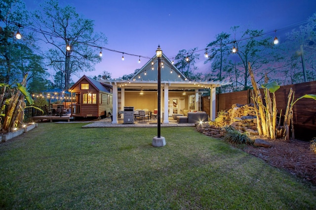 back house at dusk featuring a lawn, an outdoor living space, ceiling fan, and a deck