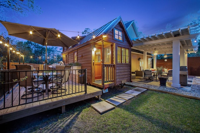 back house at dusk featuring a pergola, a deck, and a lawn