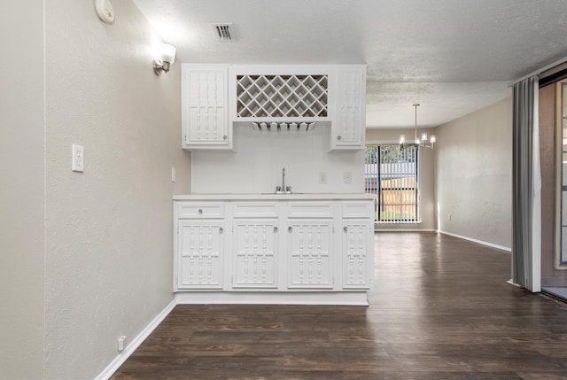 bar with decorative light fixtures, white cabinetry, dark wood-type flooring, and a chandelier