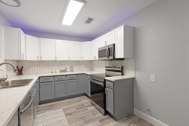 kitchen with tasteful backsplash, sink, light hardwood / wood-style flooring, and appliances with stainless steel finishes