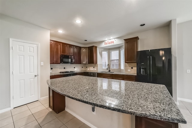 kitchen with sink, dark stone countertops, a breakfast bar, a kitchen island, and black appliances