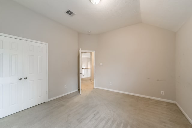 unfurnished bedroom featuring a closet, light colored carpet, and lofted ceiling