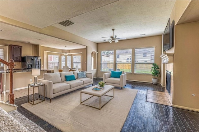 living room featuring visible vents, baseboards, a fireplace with flush hearth, a textured ceiling, and wood-type flooring