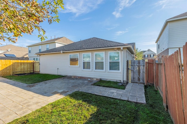 rear view of house with a patio, a fenced backyard, a shingled roof, a lawn, and a gate