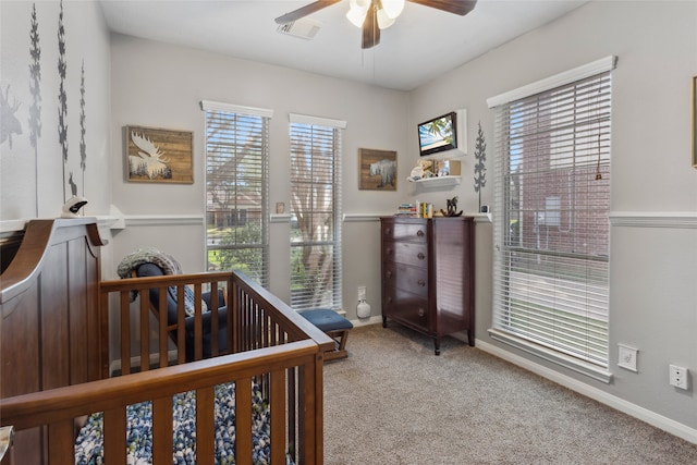 carpeted bedroom with ceiling fan and a crib