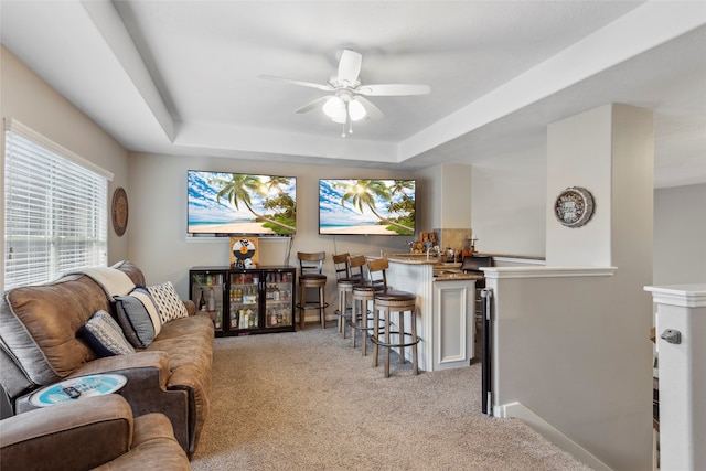 living room with a raised ceiling, light carpet, and ceiling fan