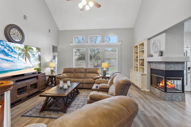 living room featuring a tile fireplace, light hardwood / wood-style flooring, high vaulted ceiling, and ceiling fan