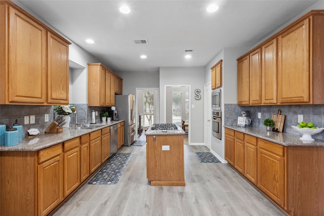 kitchen with light wood-type flooring, tasteful backsplash, light stone counters, stainless steel appliances, and a center island