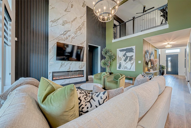 living room with wood-type flooring, a towering ceiling, an inviting chandelier, and a fireplace