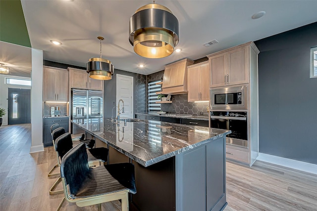 kitchen with a breakfast bar area, dark stone countertops, backsplash, stainless steel appliances, and a center island with sink