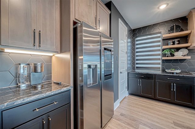 kitchen with tasteful backsplash, dark stone countertops, stainless steel fridge, and light wood-type flooring