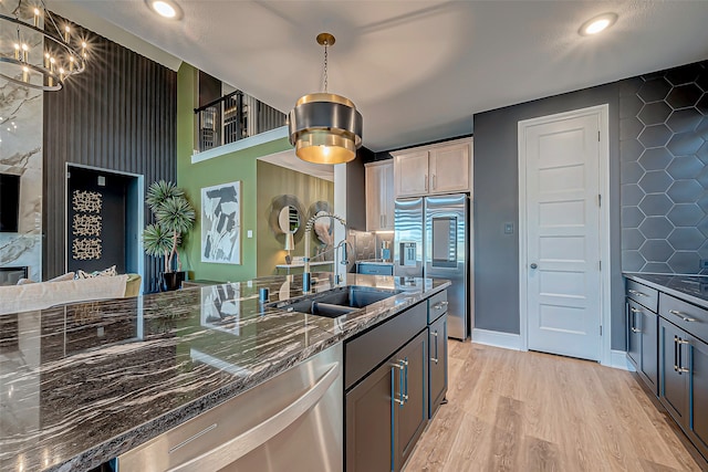 kitchen with appliances with stainless steel finishes, sink, pendant lighting, and dark stone counters