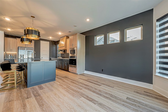 kitchen featuring a kitchen bar, hanging light fixtures, light brown cabinets, stainless steel appliances, and a kitchen island with sink