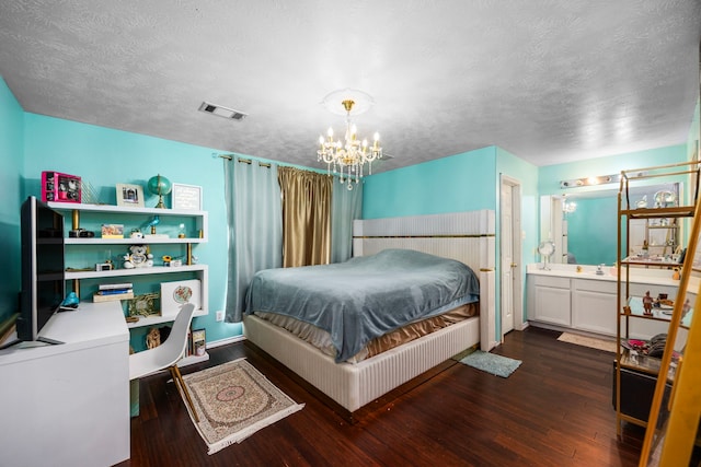 bedroom featuring ensuite bathroom, dark wood-type flooring, a textured ceiling, and an inviting chandelier