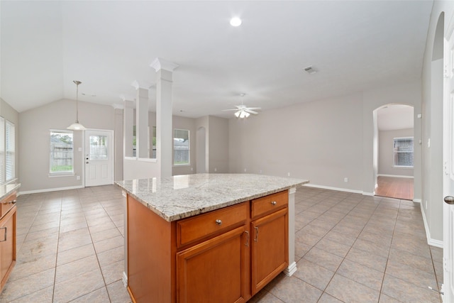 kitchen with light stone countertops, ceiling fan, a kitchen island, hanging light fixtures, and light tile patterned flooring