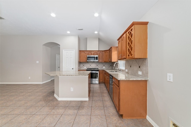 kitchen featuring lofted ceiling, light tile patterned floors, appliances with stainless steel finishes, a kitchen island, and light stone counters