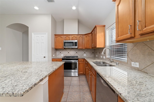 kitchen with sink, stainless steel appliances, tasteful backsplash, light stone counters, and vaulted ceiling