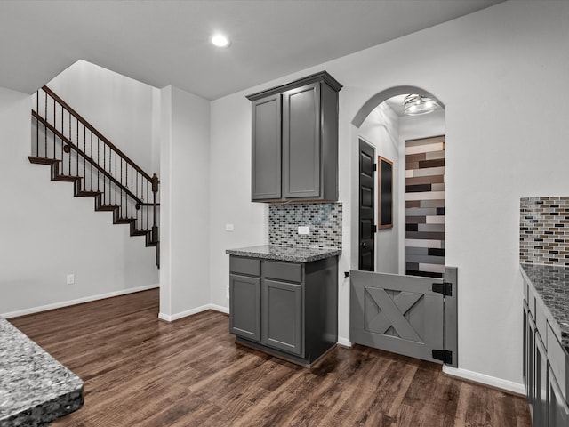 kitchen featuring tasteful backsplash, gray cabinetry, dark hardwood / wood-style flooring, and stone countertops